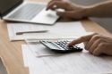 Foto: Person tippt auf Laptop und Taschenrechner